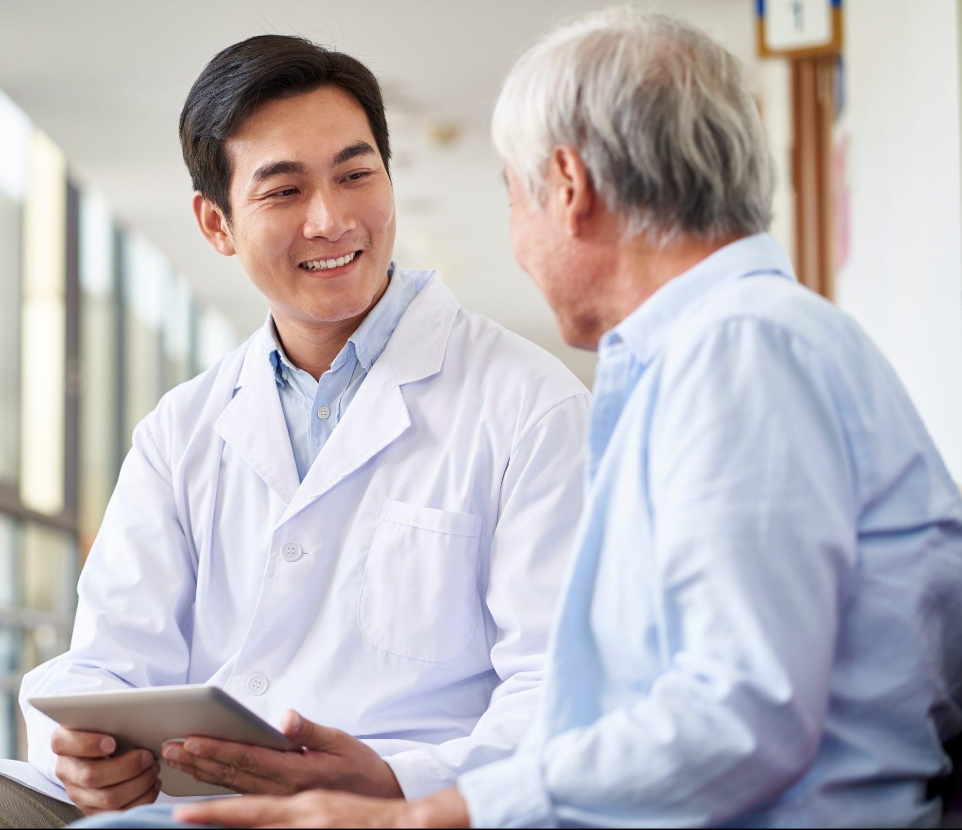 young asian doctor talking to senior man in hospital hallway