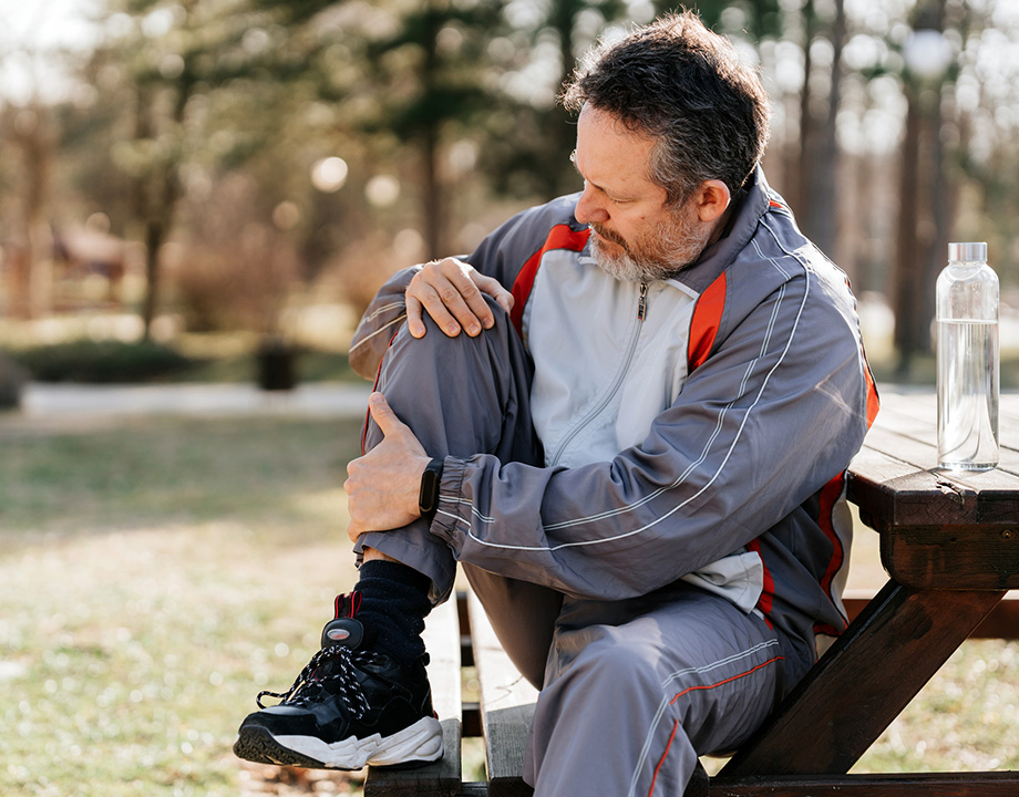 a man sitting on a bench touching his painful knee