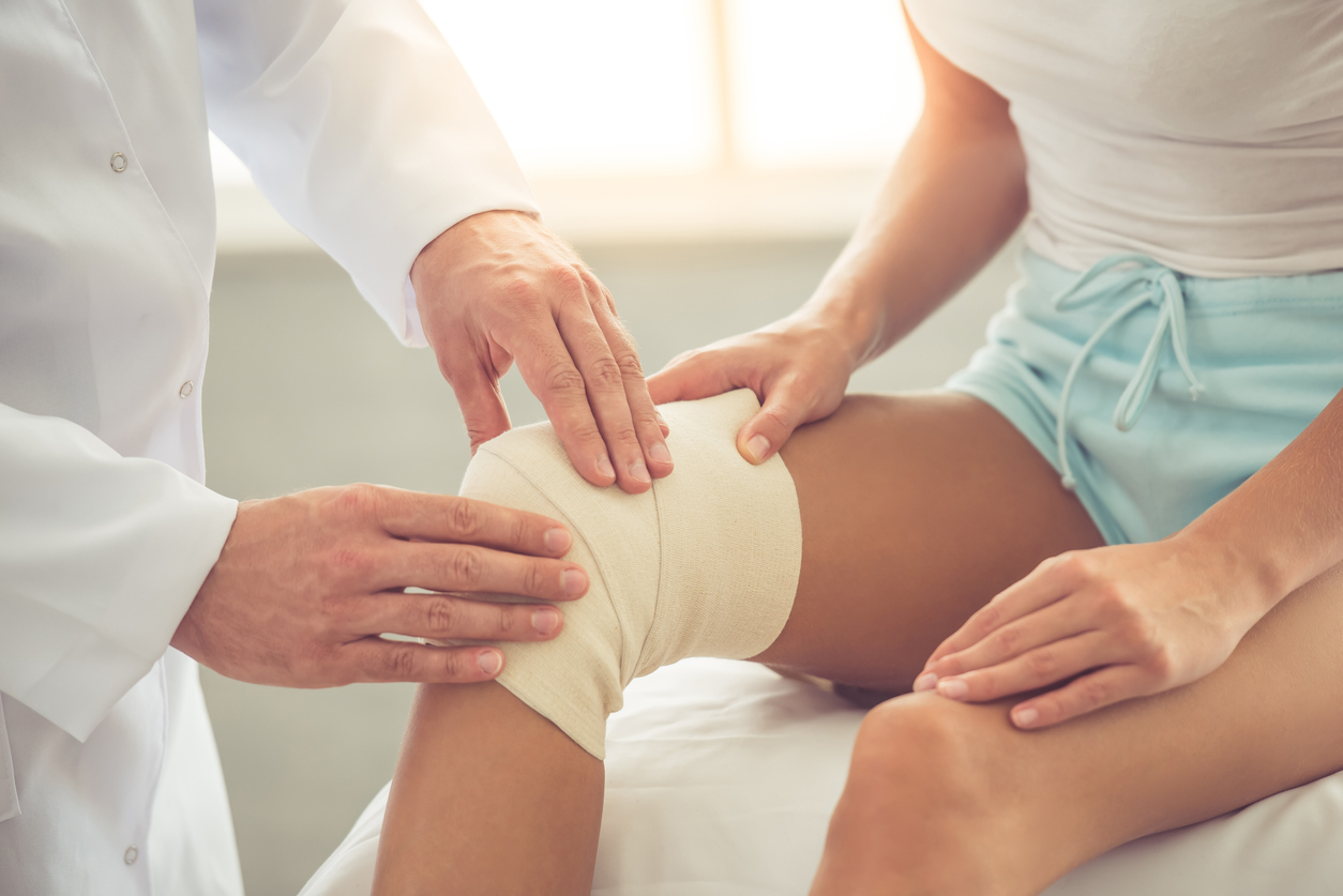 A female patient with a bandaged knee consults with an orthopedic doctor about her ACL tear