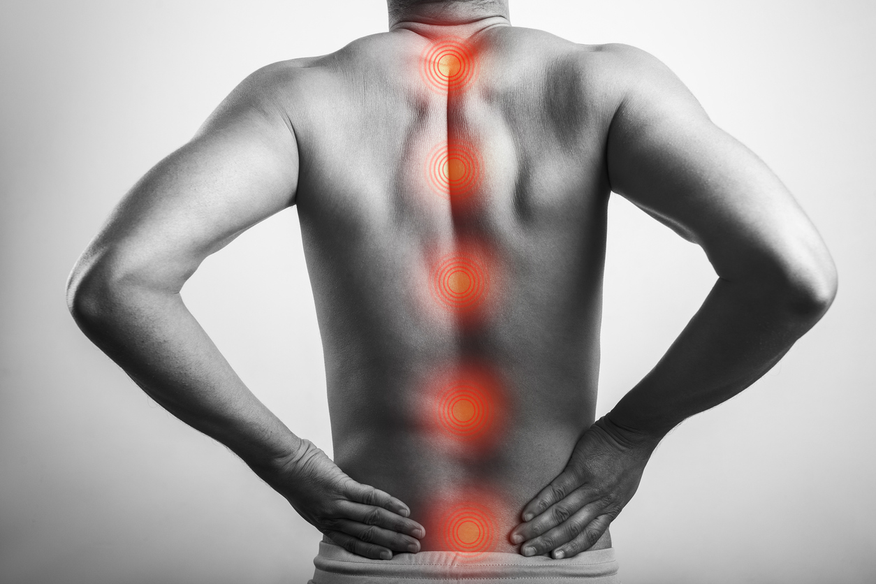 A black-and-white image of a man holding his lower back while red spots radiate along his spine