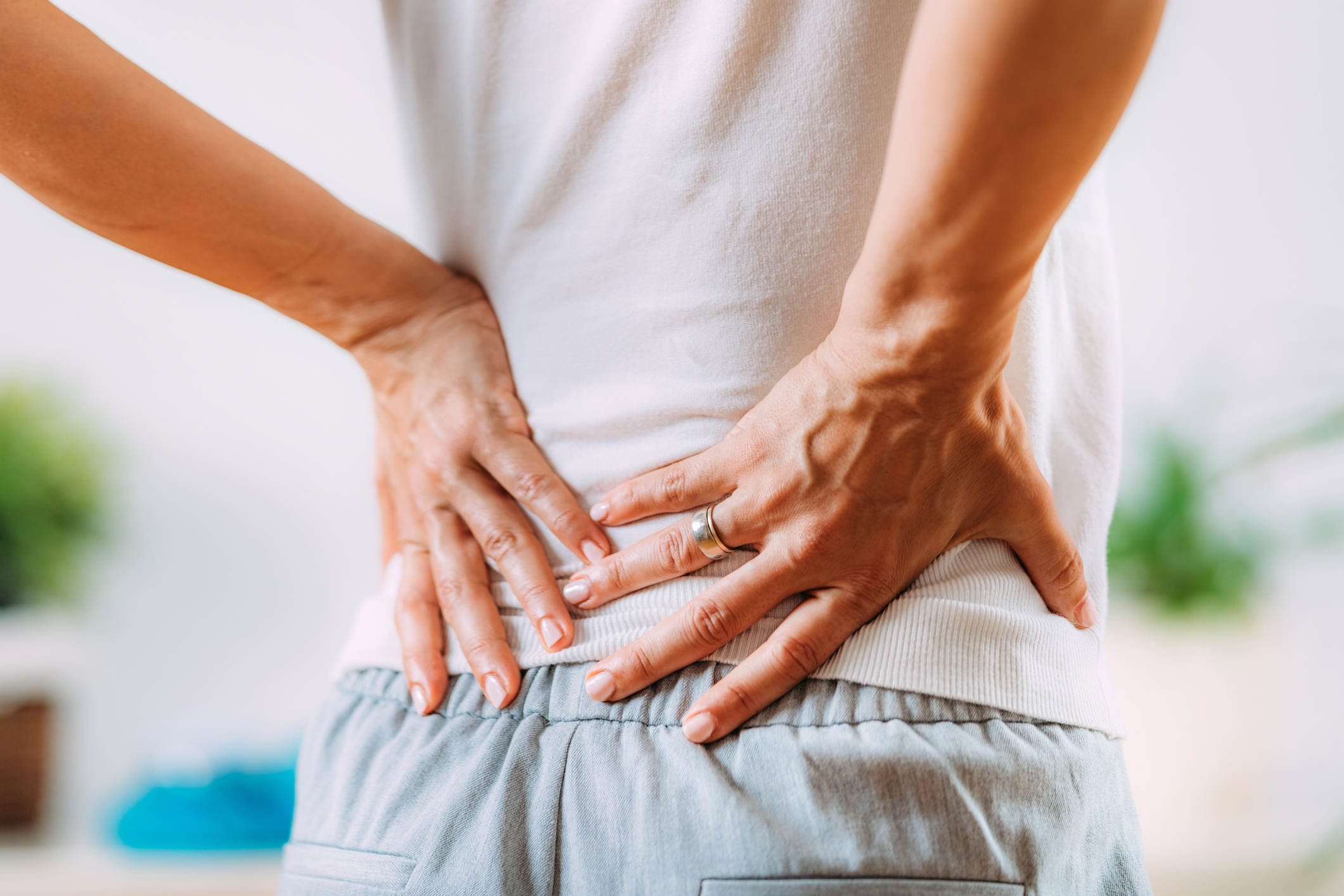 A woman stands in her living room, visibly distressed, holding her lower back due to sciatica pain.