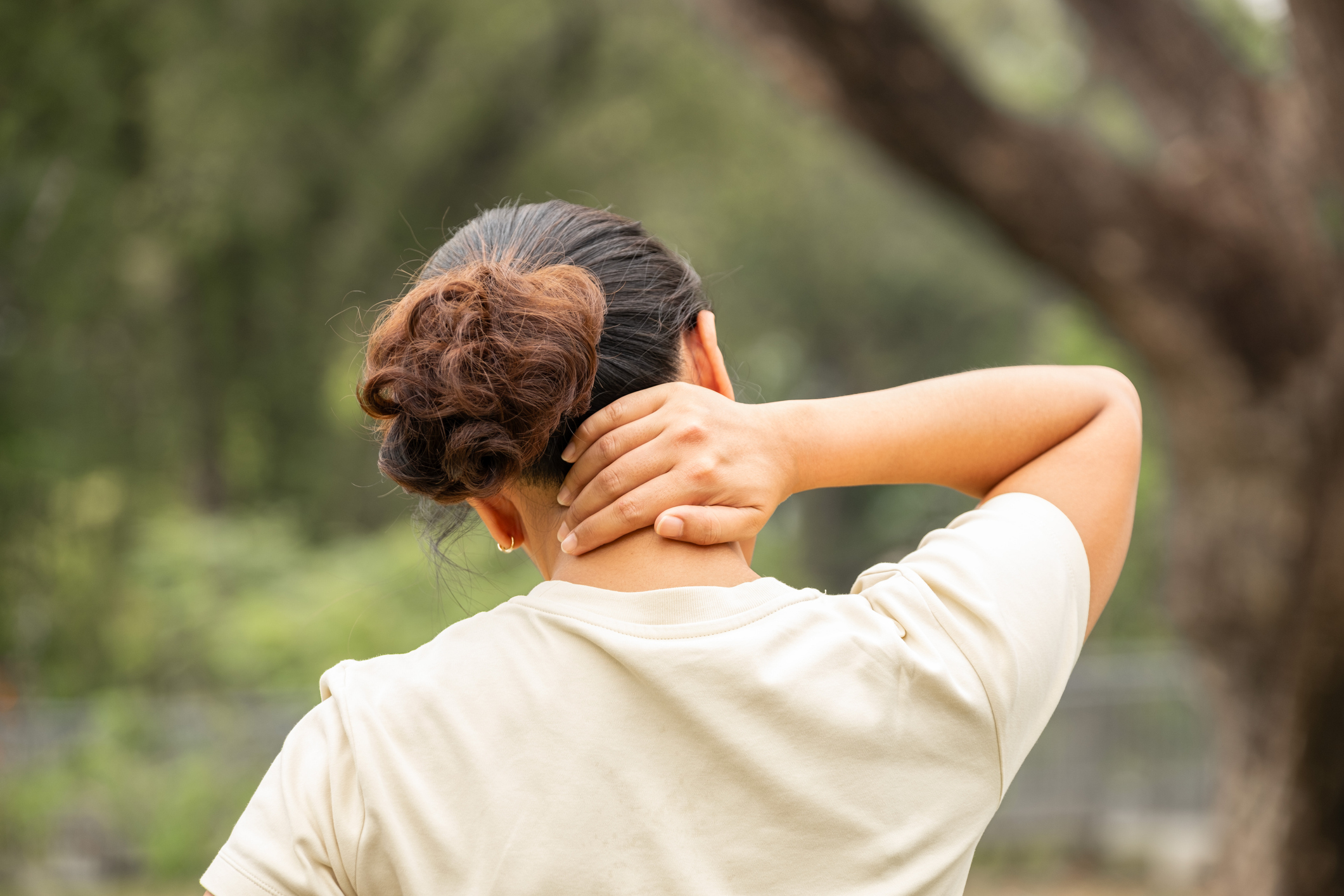 A woman holding her neck in discomfort, visibly experiencing pain as she wonders how to relieve neck pain