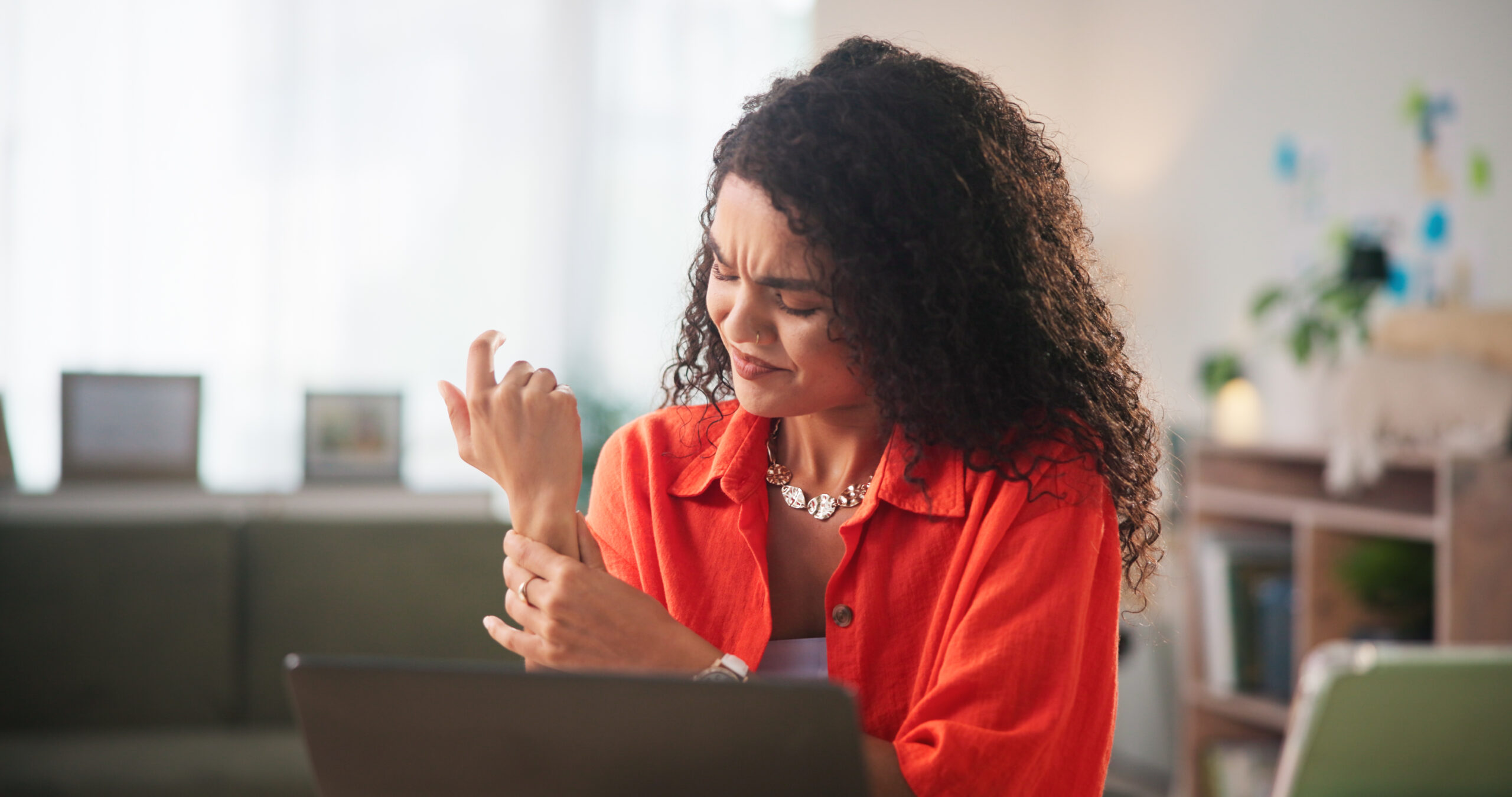 A woman sitting at a desk, touching her wrist, contemplates whether she has a sprain or fracture.