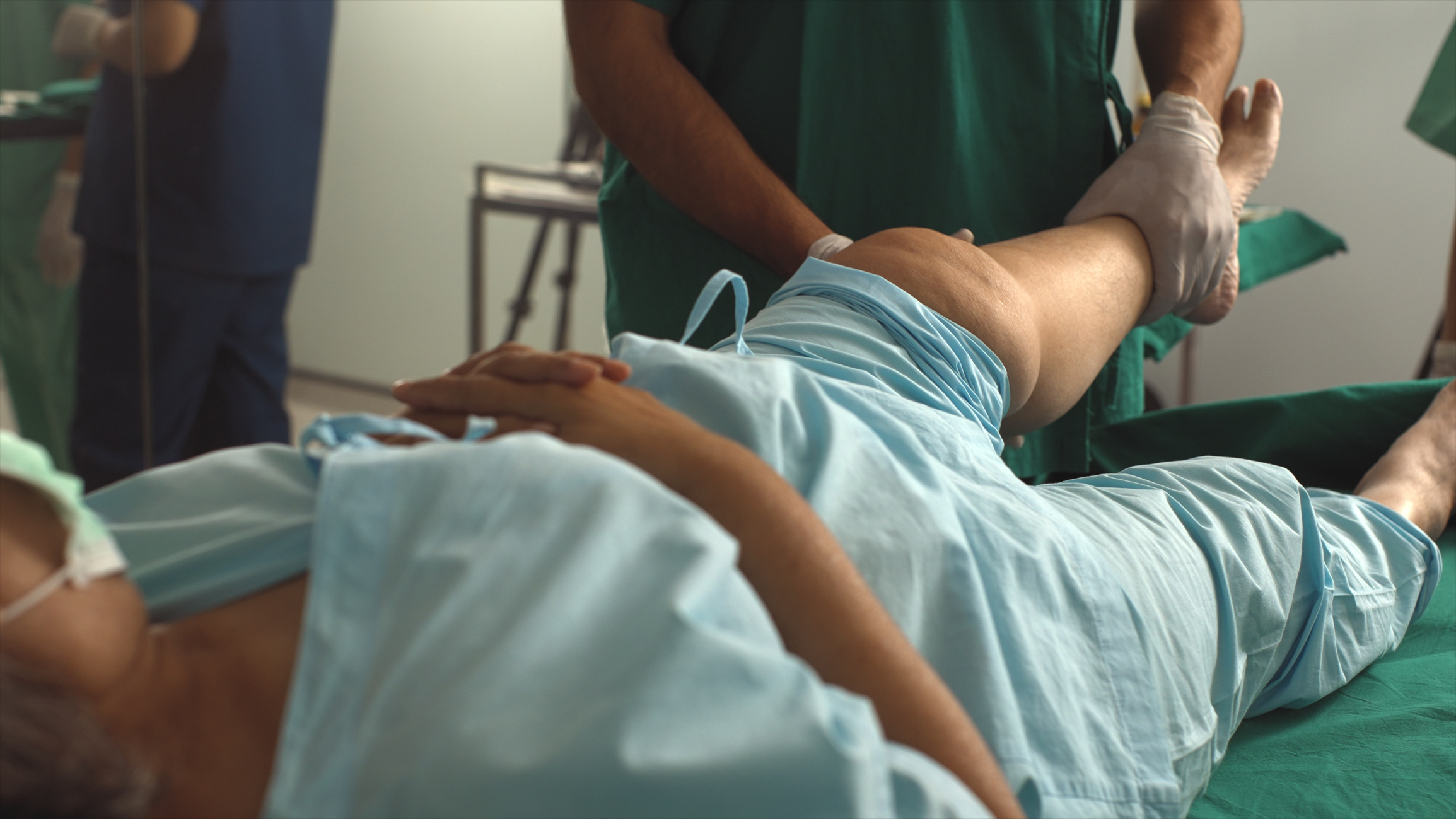 Patient in a blue hospital gown rests on a bed, getting ready for outpatient joint replacement surgery.