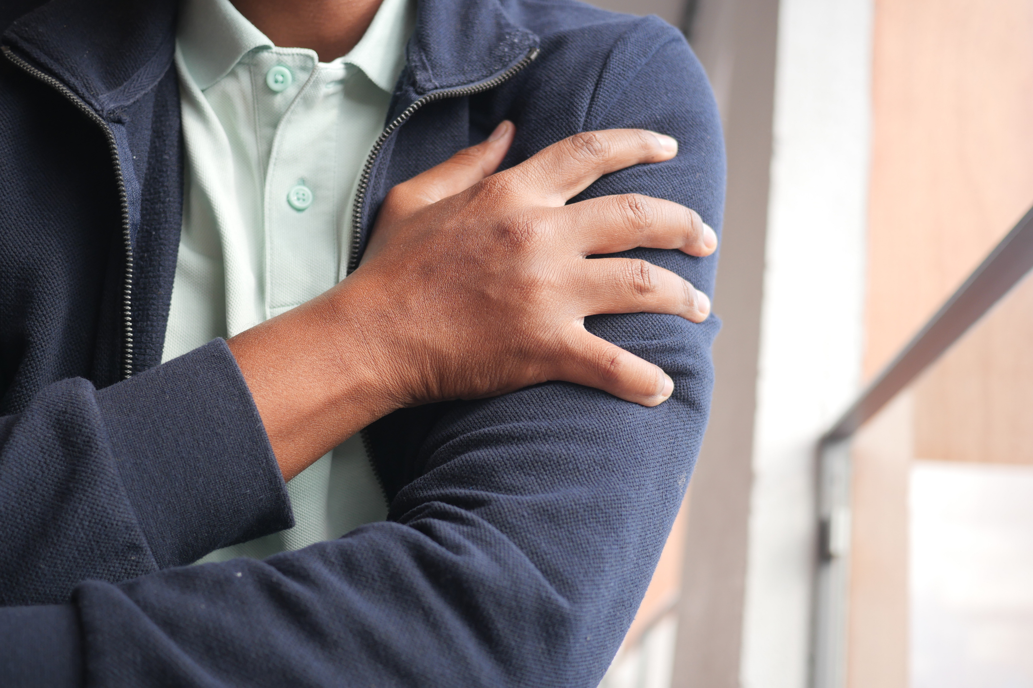 A man wearing a dark blue jacket and a light green shirt grips his left shoulder due to winter joint pain.