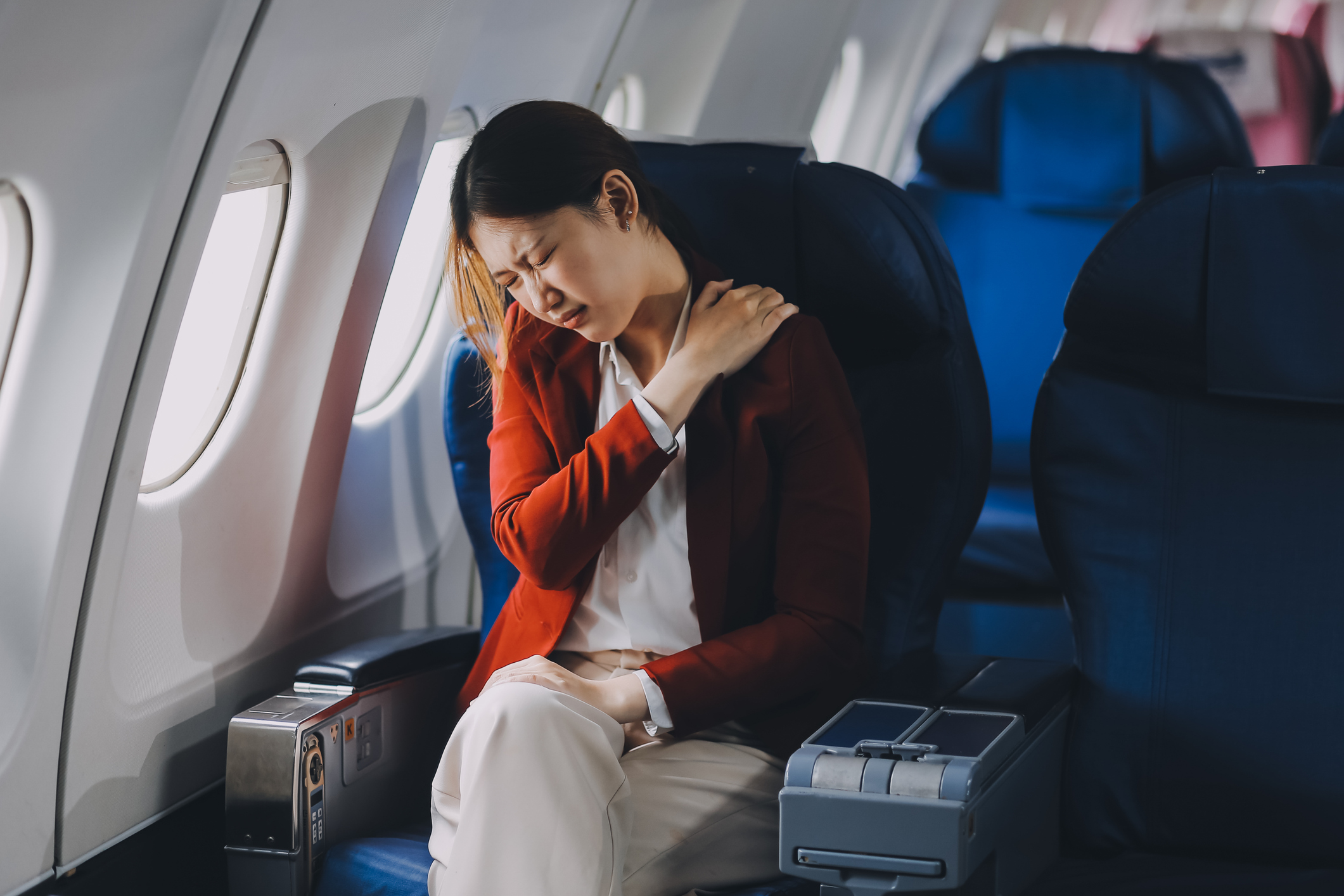 A woman is travelling with back and neck pain on an airplane.