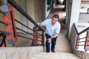 An older adult gripping a stair railing due to hip pain that limits daily activities, signaling the need for orthopedic evaluation.